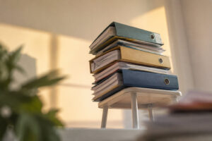 Pile de trois classeurs remplis de documents posés sur un petit tabouret blanc dans une pièce lumineuse.