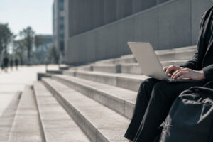 Une personne en tenue professionnelle assise sur des marches en béton travaille sur son ordinateur portable.