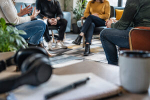 Quatre personnes assises en cercle dans un salon, avec un casque audio et un carnet au premier plan.